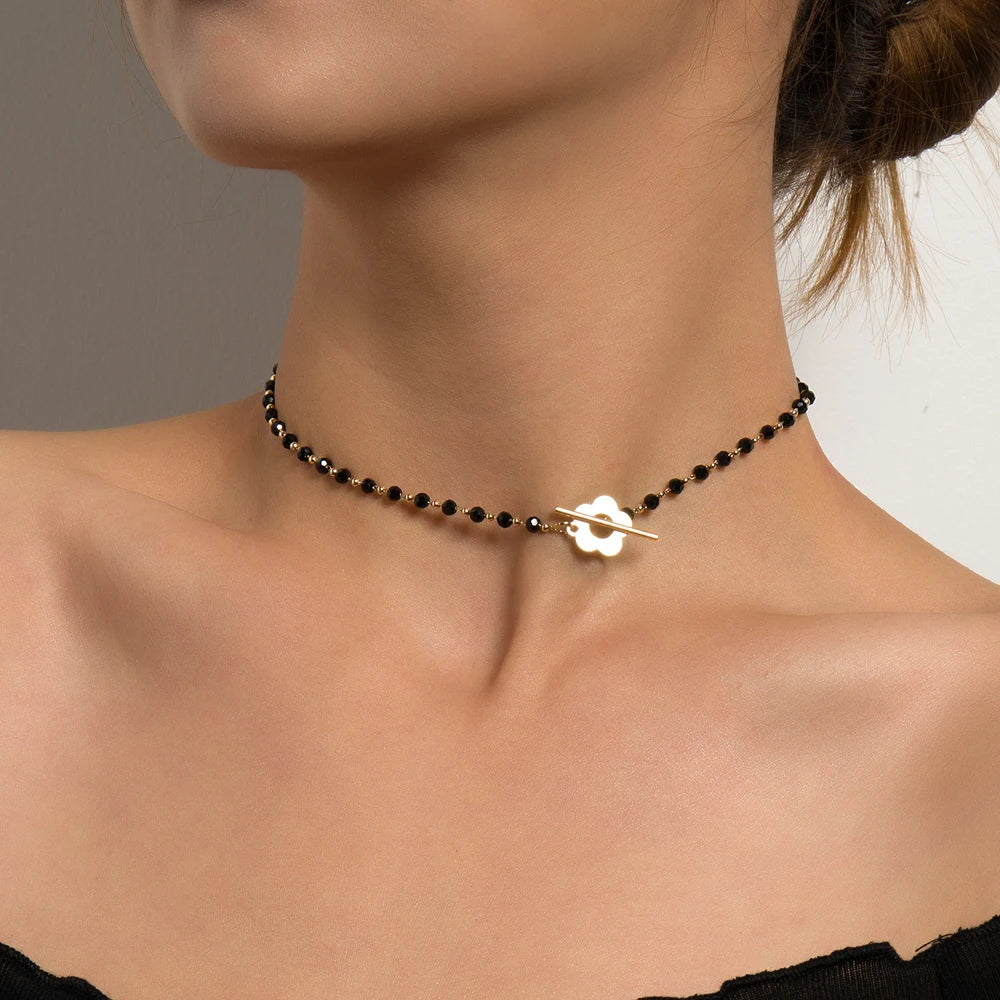 Collier ras-du-cou fleur de marguerite en plaqué or jaune et cristaux noirs porté au cou d'une femme vue de proche.