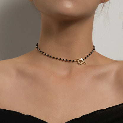 Collier ras-du-cou fleur de marguerite en plaqué or jaune et cristaux noirs porté au cou d'une femme vue de face.