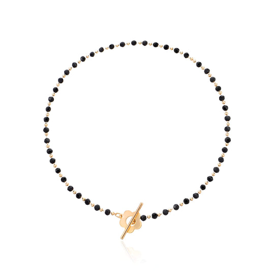 Collier ras-du-cou fleur de marguerite en plaqué or jaune et cristaux noirs sur fond blanc.