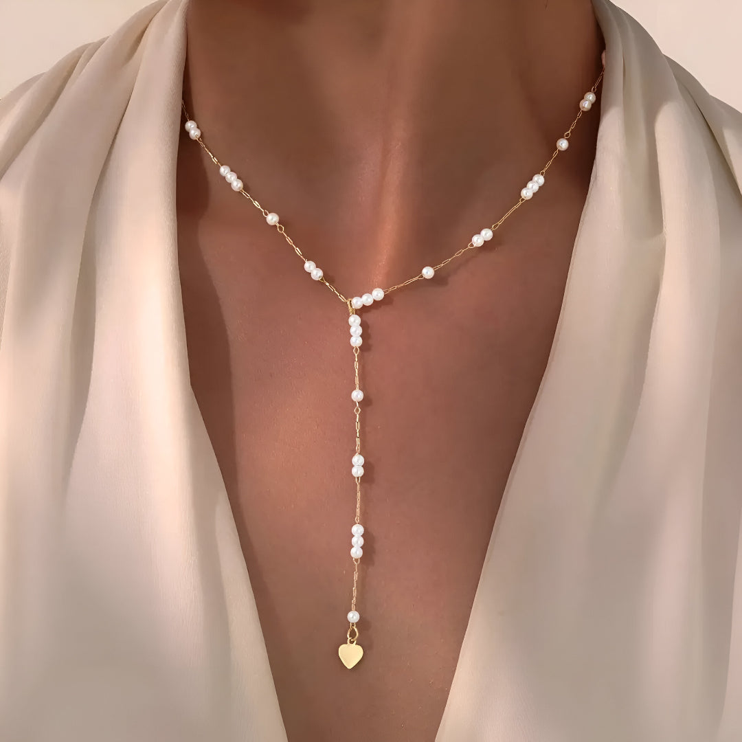 Collier sautoir fantaisie en acier doré orné de perles porté au cou d'une femme.