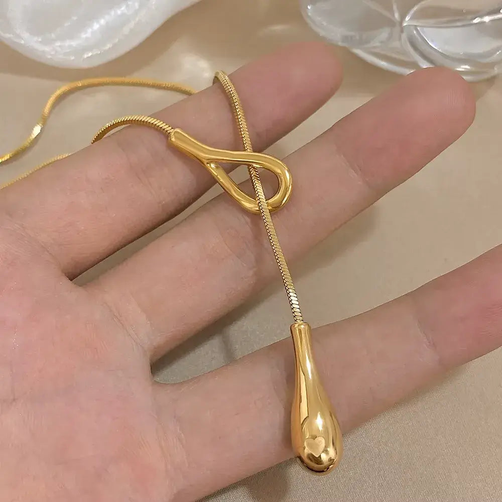 Sautoir goutte dorée amovible en acier inoxydable 316L plaqué or jaune montré sur une main de femme vue de proche.