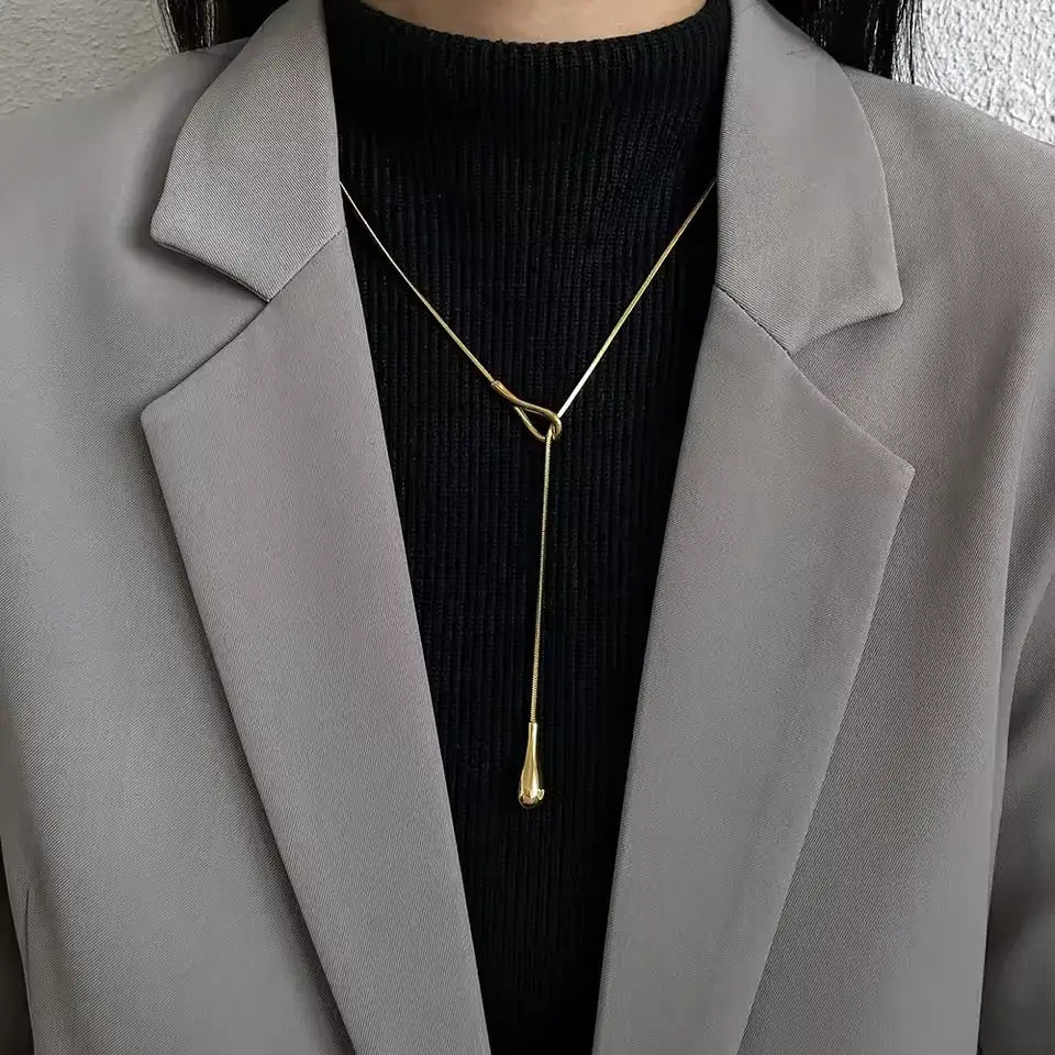 Sautoir goutte dorée amovible en acier 316L plaqué or jaune porté au cou d'une femme vue de face.
