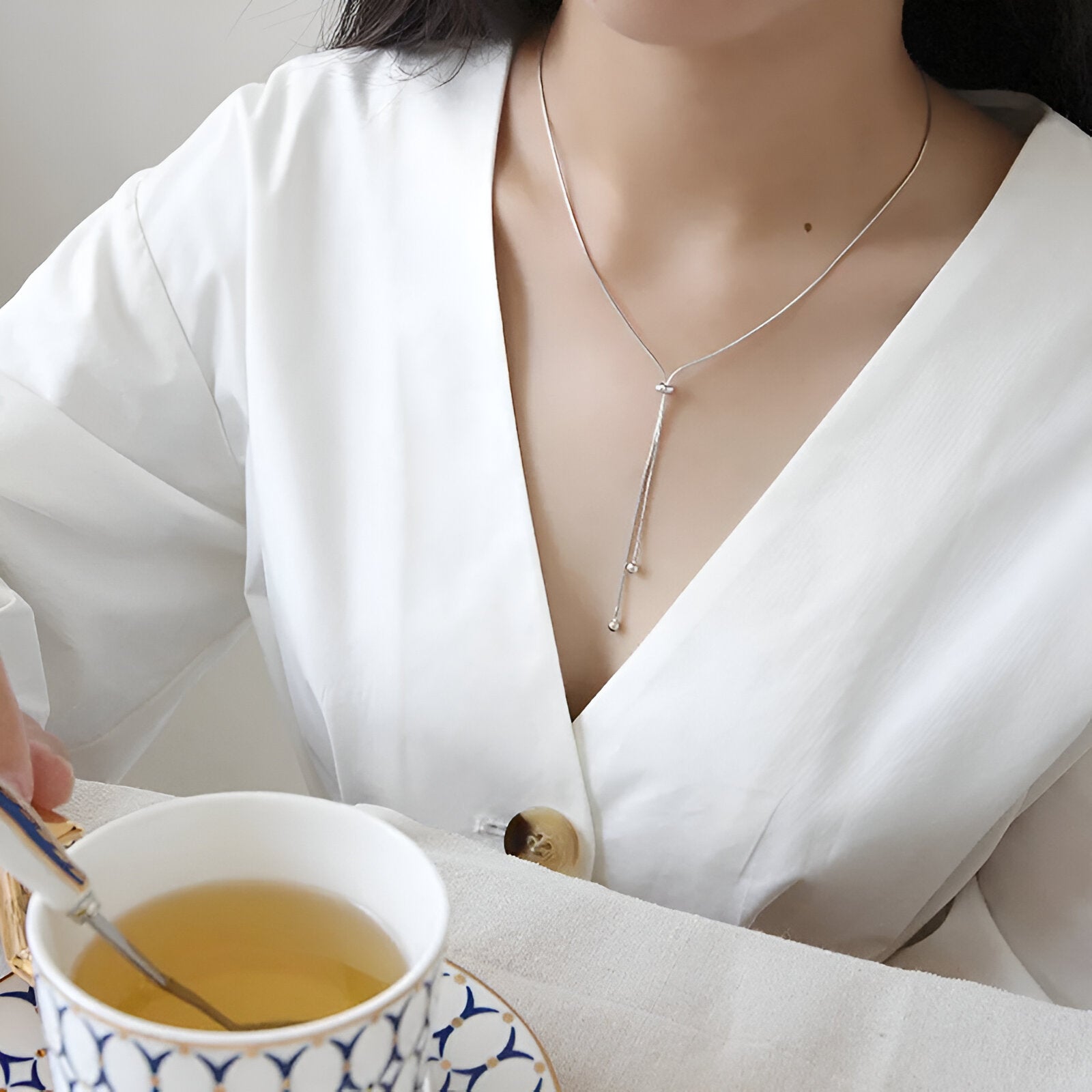 Collier sautoir perle synthétique amovible en acier inoxydable plaqué or blanc porté au cou d'une femme.