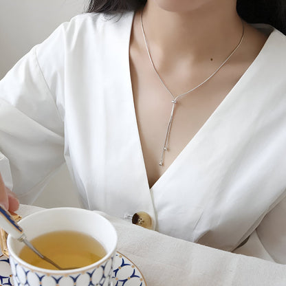 Collier sautoir perle synthétique amovible en acier inoxydable plaqué or blanc porté au cou d'une femme.